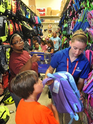 In this Wednesday, Aug. 5, 2015, file photo, Tori Smith, center, director of the Southwest Branch of the Boys and Girls Club in Wichita Falls, Texas, and employees of Academy Sports and Outdoors help several club members pick out new backpacks for school.