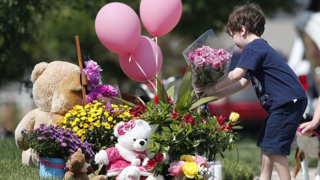 An unidentified young boy places a bouquet of flowers on a pile of tributes outside the home where a pregnant woman and her two daughters lived Thursday, Aug. 16, 2018, in Frederick, Colo. The woman's husband has been arrested in the disappearance of the woman and children. Authorities say that they have found the woman's body and believe to know the whereabouts of the two girls. (AP Photo/David Zalubowski)