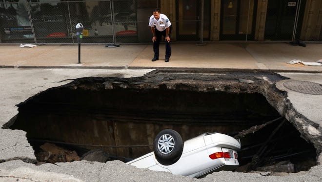 A St. Louis police officer looks over a large hole in 6th Street, Thursday, June 29, 2017, in St. Louis, that swallowed a Toyota Camry between Olive and Locust Streets. It isn't immediately clear what caused the collapse.
(Christian Gooden/St. Louis Post-Dispatch via AP)