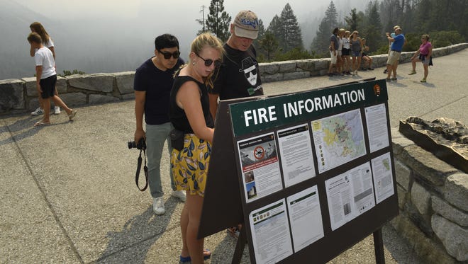 Tourists from the Netherlands read fire maps July 24, 2018, at Tunnel View in Yosemite National Park in California as smoke obscures the view.