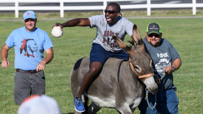 Central Academy Principal Anthony Black, center, celebrates tagging out Sarah's Angel player Sydnie Coffman, not pictured, on first base during the Donkey Softball match at the Henderson County Fairgrounds in Henderson, Ky., Saturday, July 7, 2018. Sam Skaggs, right, helped pull Black's donkey around the field to help the Swamp Donkeys defeat Sarah's Angels 11-6. 