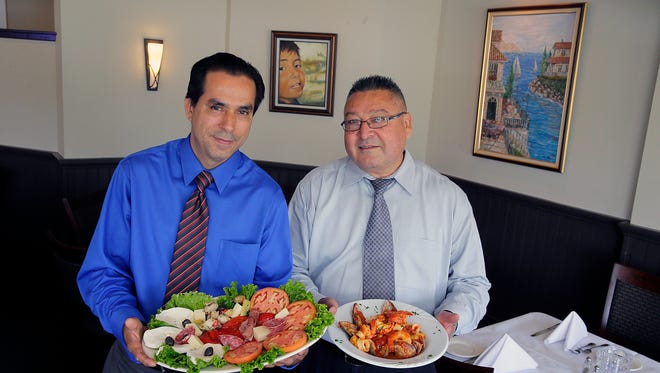 Nelson Monroy (left) and Ciro A. Bojaca, two of the owners of Villa Vittoria, hold a plate of antipasto Vittoria and a plate of zuppa di pesce in the dining room of their restaurant, which reopened in August following a 2016 fire.