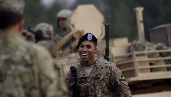 An unidentified U.S. Army soldier smiles while joining his comrades in front of an Abrams M1 tank during a live round shooting exercise of U.S. Army's 1st Cavalry Division, 1st Brigade Combat team Unit "Ironhorse" at the training area of the Military Base in Adazi, Latvia, Nov. 6, 2014.