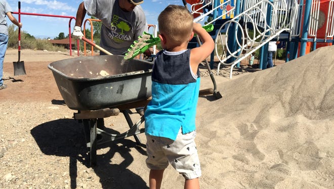 Jax Carr, 2 years old, helps his dad spread sand on the playground of Pauite Park.