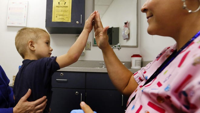 A 4-year-old sitting on his mother's lap gets a high five from an RN Tania Golden at the Columbus Public Health Department in 2013. He was catching up on immunization shots.
