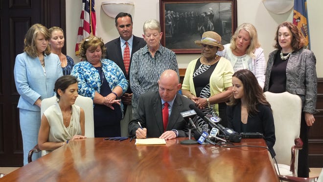 Delaware Gov. Jack Markell on Tuesday signs a law, named for the late Attorney General Beau Biden, that strengthens background check requirements for child-serving entities. He is seated next to Beau Biden's widow, Hallie, left, and Biden's sister, Ashley.