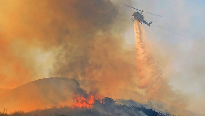 A Ventura County Fire helicopter makes a water drop on an oil field service road while working a wildfire in Ventura County, Calif., Dec. 26, 2015. Federal officials said Tuesday that they don't expect this year's wildfire season to be as severe.