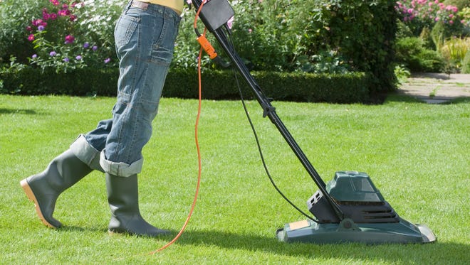 Woman mowing with electric mower.