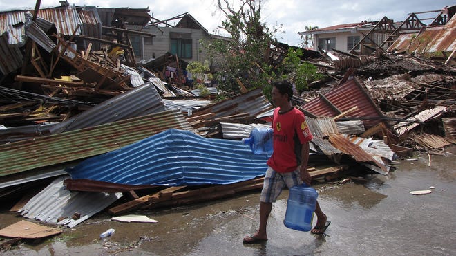 A man carries a containers of water past destroyed homes in Ormoc, Phiippines.