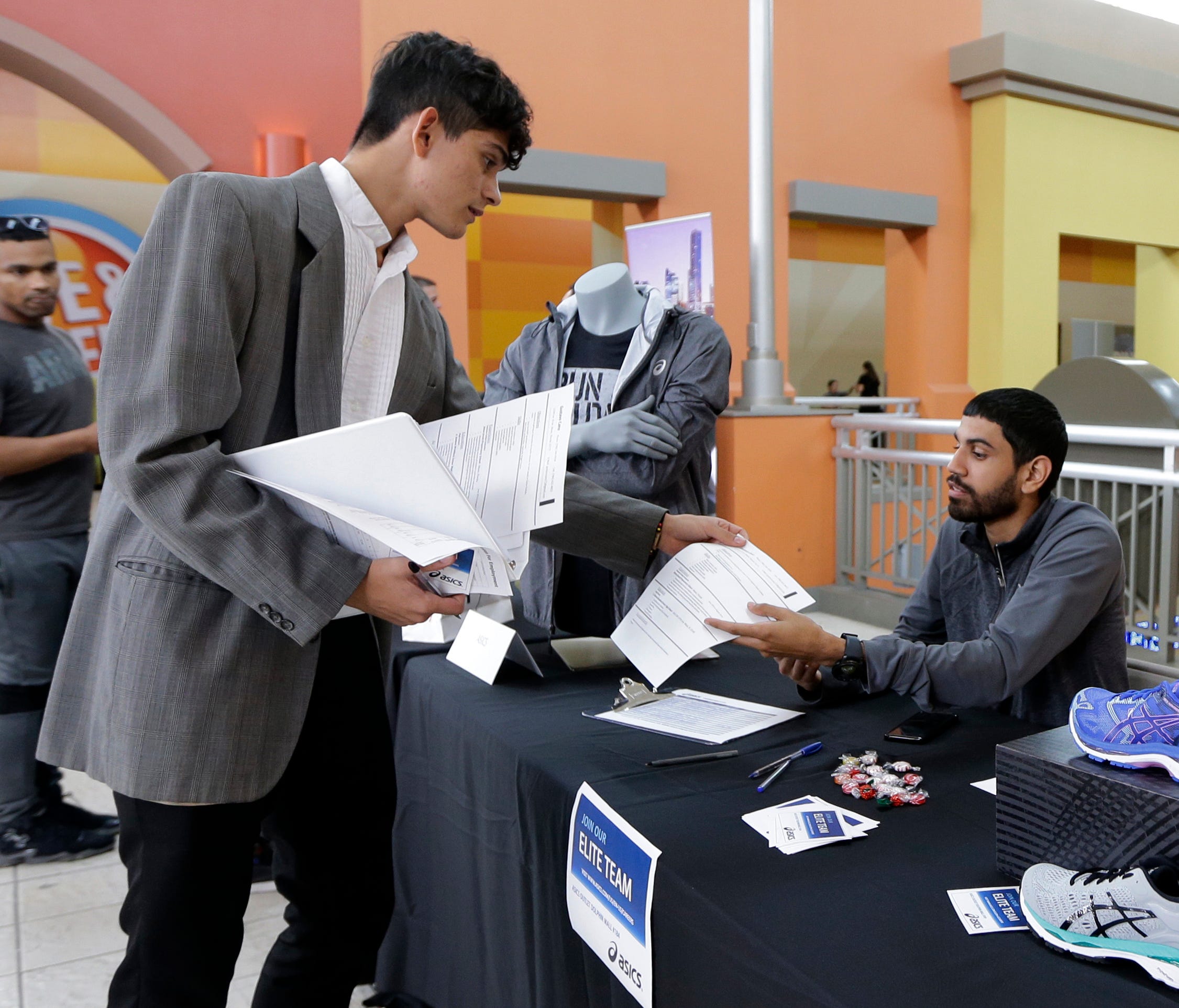 In this Tuesday, Oct. 3, 2017, photo, job seeker Gustavo Cano, left, hands his resume to Javier Torres at a job fair at the Dolphin Mall in Sweetwater, Fla. On Thursday, Oct. 26, 2017, the Labor Department reports on the number of people who applied 