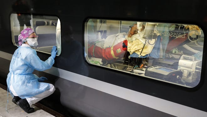 A member of the medical staff watches from the platform as a patient infected with the COVID-19 virus is lays in a train at the Gare d'Austerlitz train station, Paris, Wednesday April 1, 2020. France is evacuating 36 patients infected with the coronavirus from the Paris region onboard two medicalized high-speed TGV trains. The patients, all treated in intensive care units (ICU), are being transferred to several hospitals in Brittany, as western France is less impacted by the epidemic. The new coronavirus causes mild or moderate symptoms for most people, but for some, especially older adults and people with existing health problems, it can cause more severe illness or death.