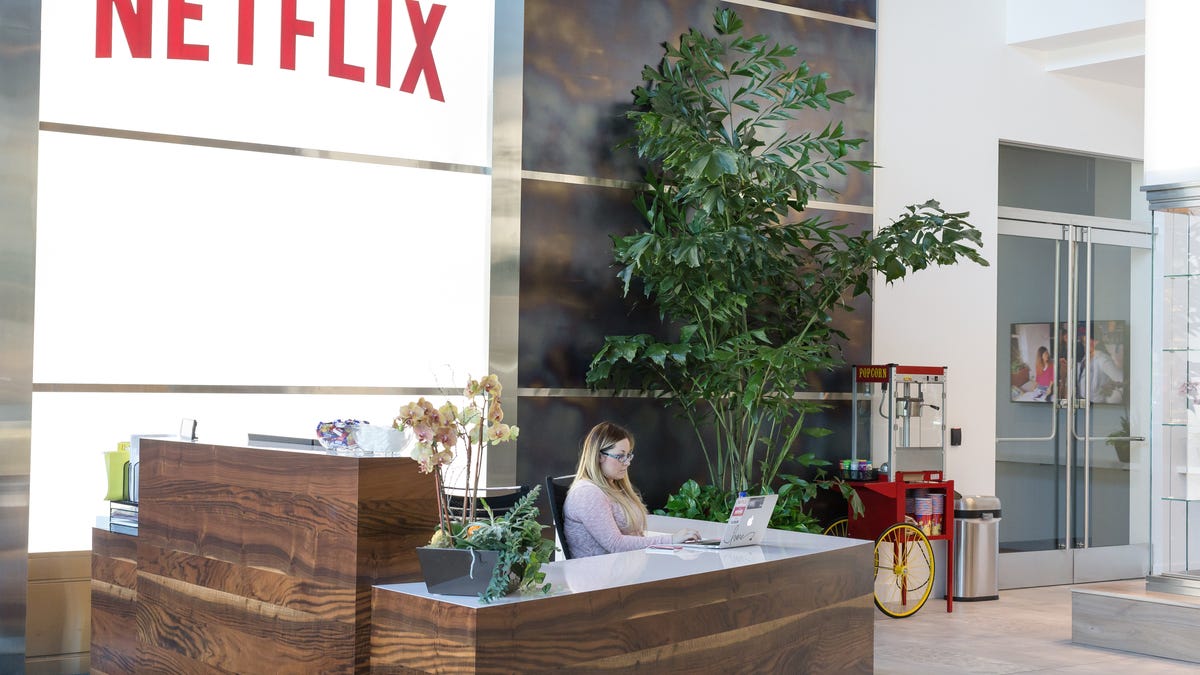 Person sitting at a reception desk. The Netflix logo is in the window above.