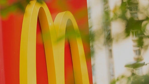 Detail of McDonald's red and yellow signage behind leafy, blurred foreground.