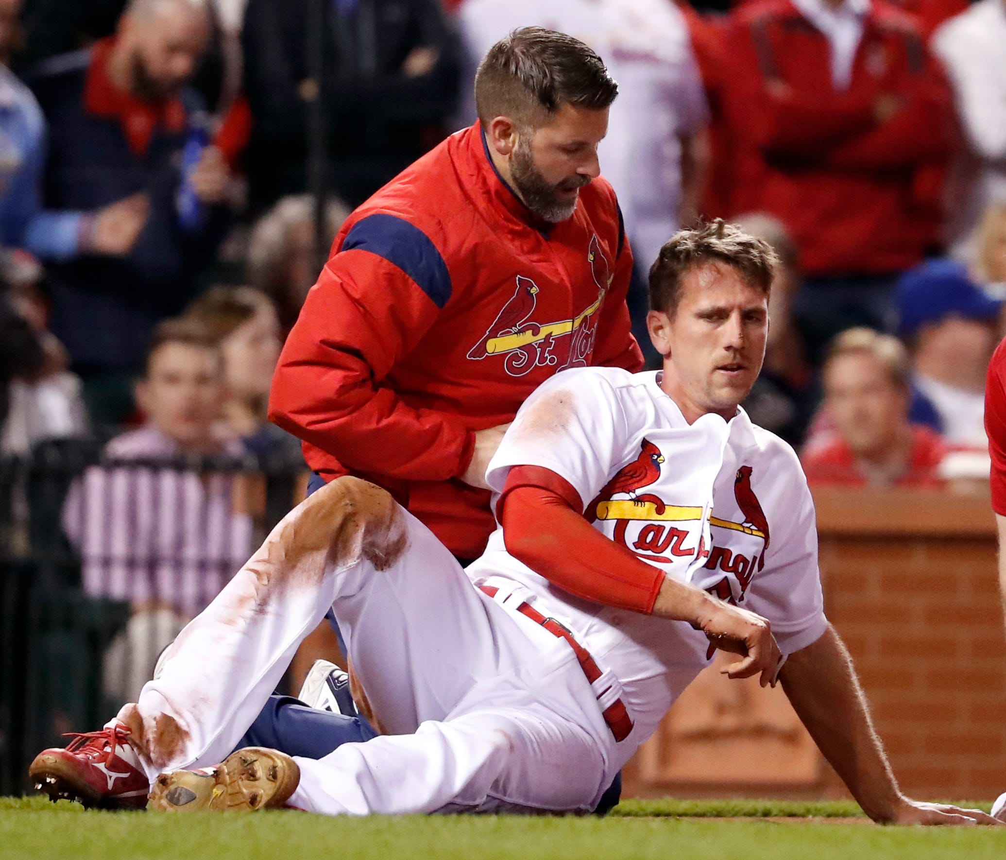 Stephen Piscotty, front, is helped by a trainer after being hit in the head with a ball while scoring during the fifth inning.