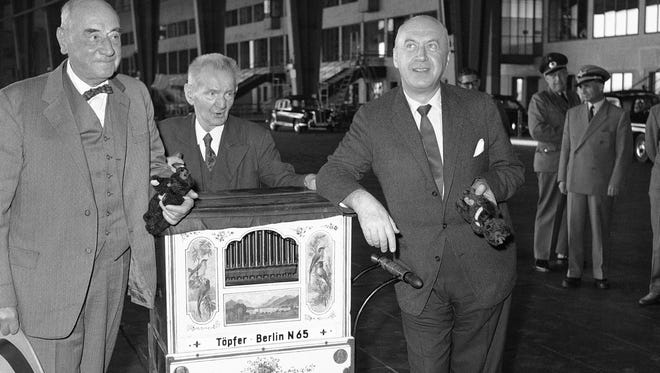 Hollywood producer and film director Otto Preminger, left, traveled to West Berlin to attend the European premier of his film "Anatomy of a Murder."  Preminger was accompanied by attorney Joseph N. Welch who plays a leading role in the film.  Between them is one of the last of the organ grinders which are gradually disappearing from the streets of Berlin.