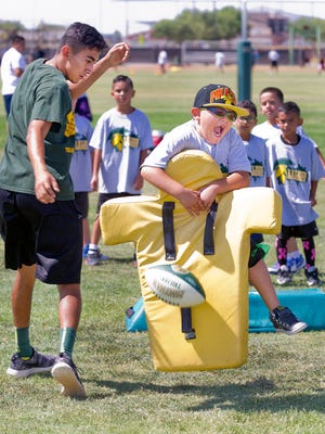 Evan Hernandez, 6, of Las Cruces hits the tackling pad with enthusiasm and knocks the ball loose as Mayfield junior Fabian Benavidez runs the "scoop and score" drill Tuesday morning at the Jim Bradley Football Camp.