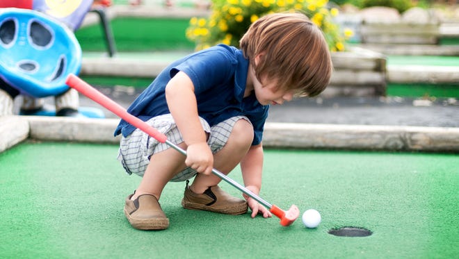 Little boy playing mini golf.