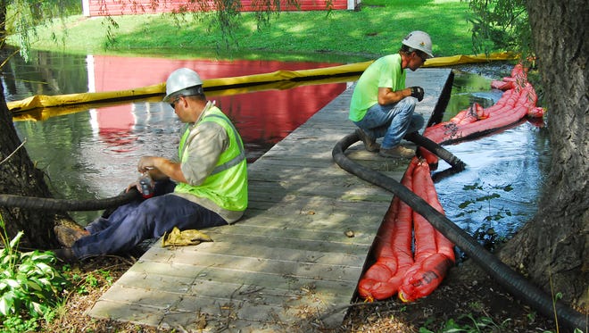 Workers siphon off oil while a boom holds back the Talmadge Creek where it flows into the the Kalamazoo River near A Drive North in Marshall Township after the oil spill.