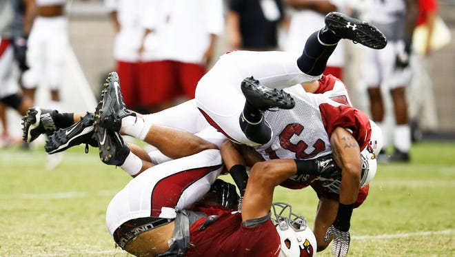 Cardinals tight end Rob Housler (bottom) is tackled by Andre Walters (front) and Lorenzo Alexander at training camp Monday, July 28, 2014 at University of Phoenix Stadium in Glendale.