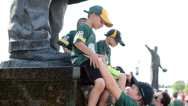 
Bryce Jansen, 12, helps Ben Micke, 6, down from the statue of Vince Lombardi in the Harlan Plaza after taking a group picture Saturday before Packers Family Night at Lambeau Field. 
