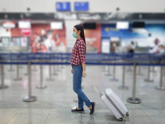 A traveler with a mask on walks through an airport.