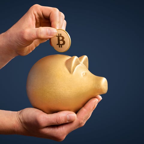 Person putting a bitcoin into a gold piggy bank.