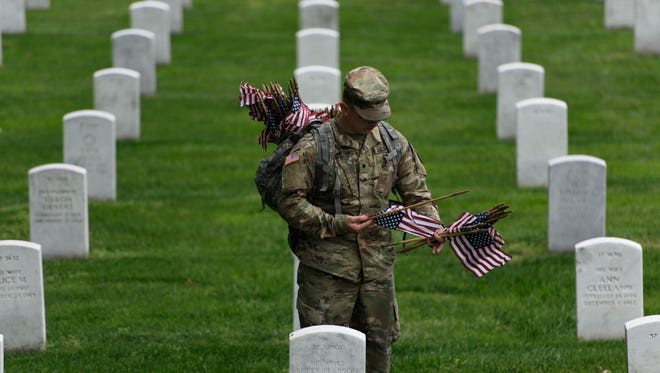 A member of the US Army places an American flags on a grave at Arlington National Cemetery.