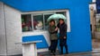 Women shelter from the rain under an umbrella in front