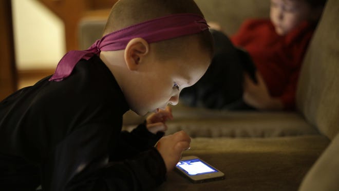 Nolan Young, 3, front, looks at a smartphone while his brother Jameson, right, 4, looks at a tablet at their home, in Boston in this 2014 file photo. A Colorado man seeks to ban the sale of smartphones to be used by children younger than age 13.