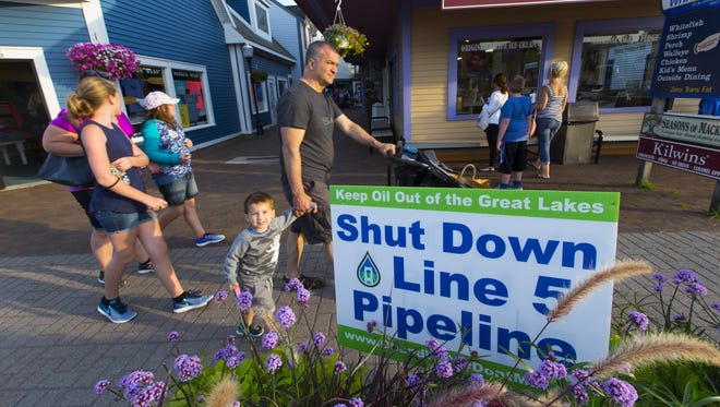 Tourists stroll past a sign opposing Enbridge Line 5 in July, 2017 in Mackinaw City.