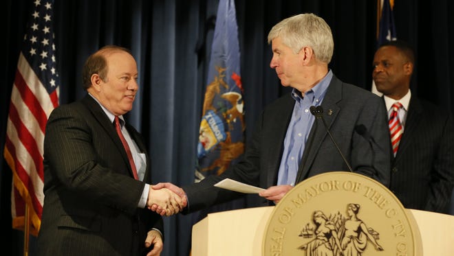 Detroit Mayor Mike Duggan, left, accepts a check from Michigan Governor Rick Snyder, as outgoing Detroit emergency manager Kevyn Orr, back right, watches during Press conference to announce the City of Detroit's exit from bankruptcy at the Public Safety Headquarters in Detroit on Wednesday, December 10, 2014.