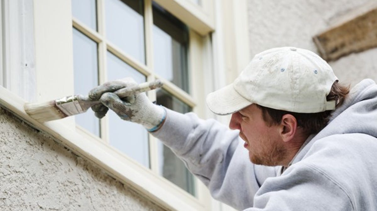 A man applies paint to trim beneath a window.
