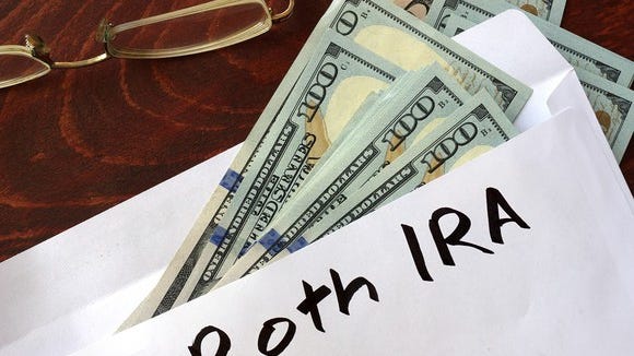 Envelope marked Roth IRA with $100 bills in it, and eyeglasses nearby.