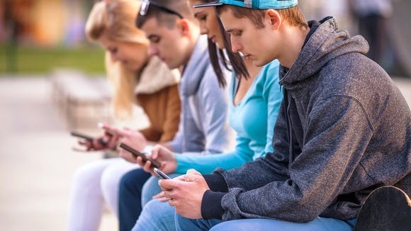 Row of teenagers all looking at their smartphones