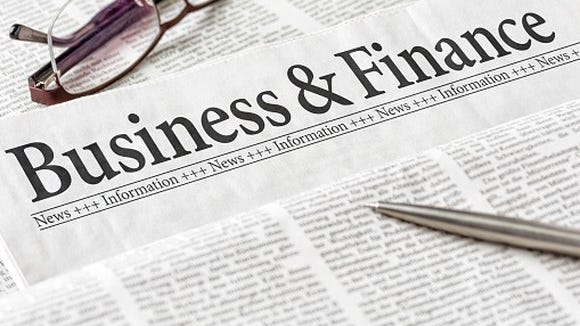 Close-up of the business and finance section of a newspaper, with a pen and a pair of glasses.