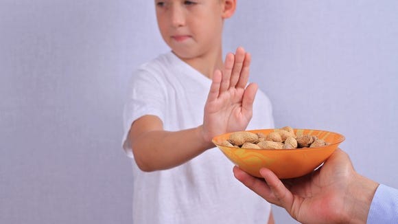 A child sticking their hand out to refuse a bowl of peanuts.