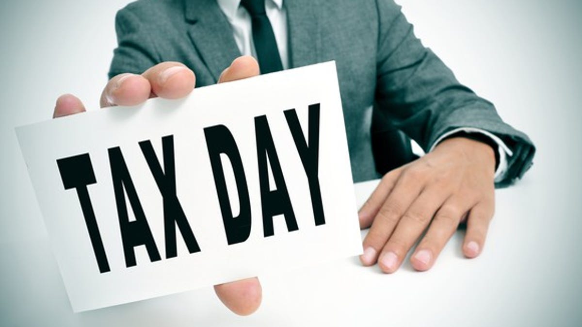 A man in a suit holding up a sign that reads, Tax Day.