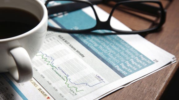 Cup of coffee and set of glasses sitting on top of a stock market graph in a newspaper.