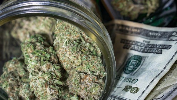 A jar of cannabis lying atop a small pile of cash.