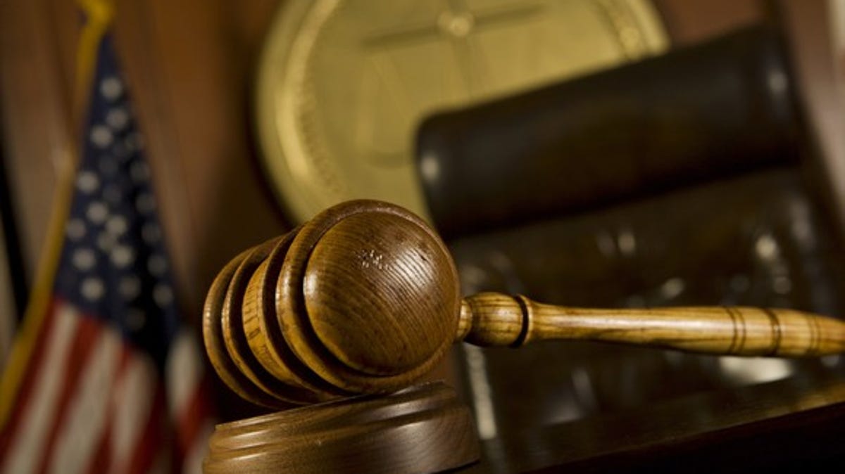 A judge's gavel and chair in the foreground of a courtroom.