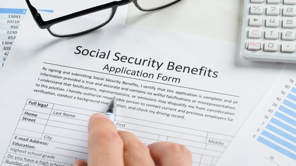 A Social Security benefits application form next to eyeglasses, a calculator, and a hand with a pen.