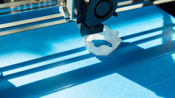 Close-up of a 3D printer printing a small, white plastic object on a blue surface.
