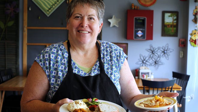 Wanda Thompson holds a plate of melted cheese and pastrami on rye, twice-baked potato melt, sweet potato melt, and cucumber- roasted pepper salad, and serving of peach cobbler.