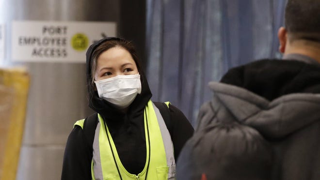 A airport agent, who declined to be identified, wears a protective mask as she waits to assist international travelers at SeaTac International Airport, Monday, Feb. 24, 2020, in SeaTac, Wash. Few travelers or workers were taking such precautions at the airport Monday, but a new virus is taking aim at a broadening swath of the globe, with officials in Europe and the Middle East now scrambling to limit it. The number of people sickened by the coronavirus topped 79,000 globally, and wherever it sprung up, officials rushed to try to contain it.