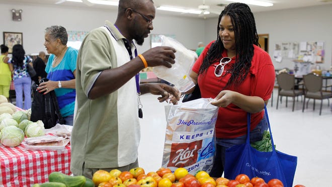 Christian Easton, right, of Shively, buys chicken from farmer Anwar Barbour on her trip to pick up fresh fruit and vegetables at the Shawnee Neighborhood Fresh Stop, held at Redeemer Lutheran Church . She has relied on food stamps for several months while her husband was laid off.