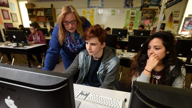 Farmington High School yearbook adviser Erin McGinley, left, helps sophomore Traedan Allison, center, with a page he is designing for the yearbook on Jan. 27 as senior Alisha Salas watches.