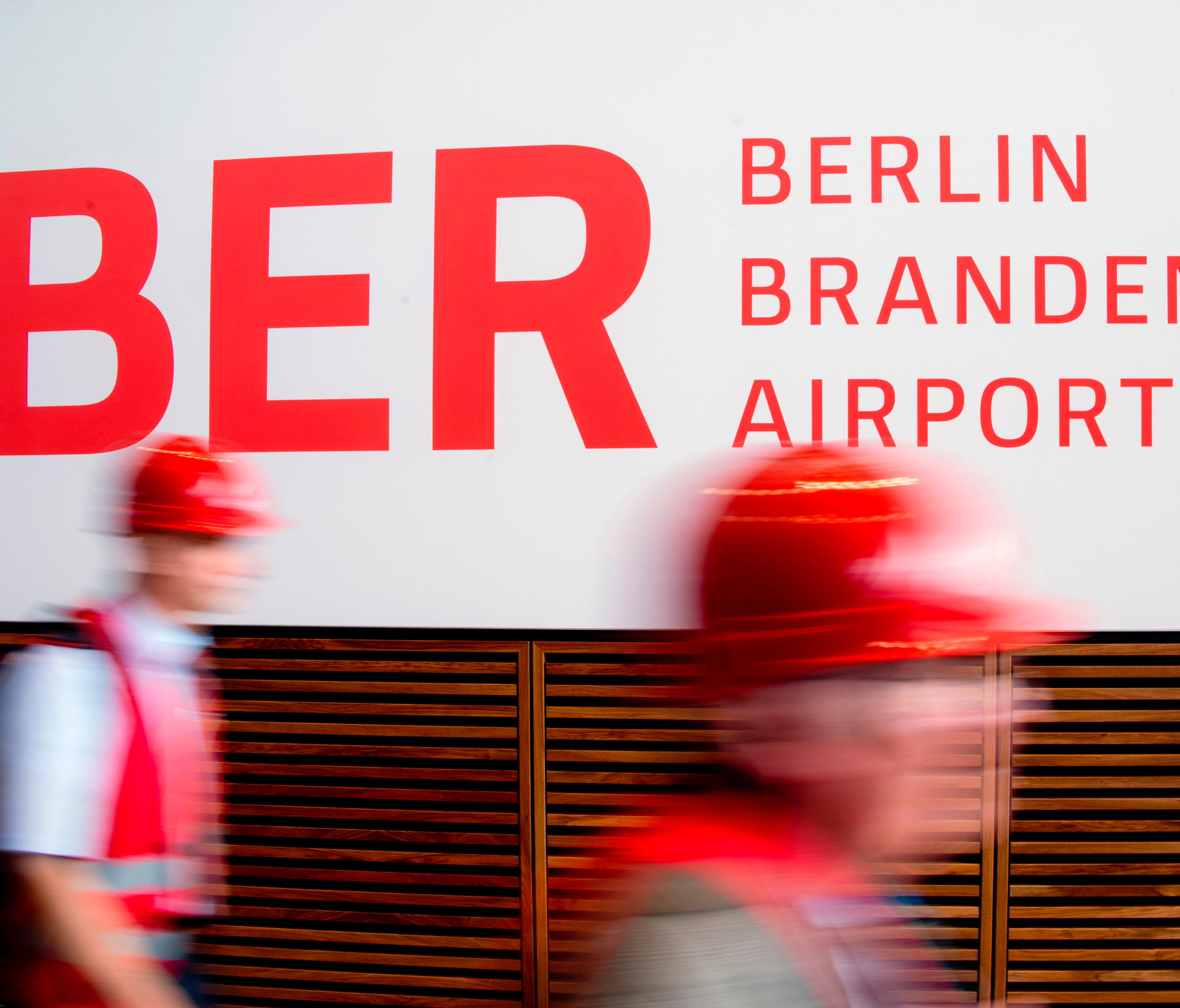 This file photo from Sept,   11, 2012, shows people wearing hard hats walk past a sign reading the name of the yet-to-open Berlin Brandenburg International Airport (airport code BER).