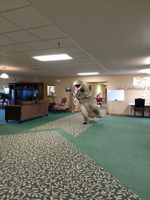 A person in a dinosaur costumes trick-or-treats at Prairie Ridge Assisted Living as part of an event organized by Waupun Senior Democratic Seminar students.