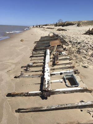 In a Saturday, April 22, 2017 photo, a portion of the hull of The Tica, a Traverse City-based vessel, is visible along the shoreline as debris from the ship, which broke up after it was grounded April 15 when it began taking on water. Authorities have closed the beach of Ludington State Park after the grounded, stranded pleasure boat broke apart just offshore. (Patti Klevorn/Ludington Daily News via AP)
