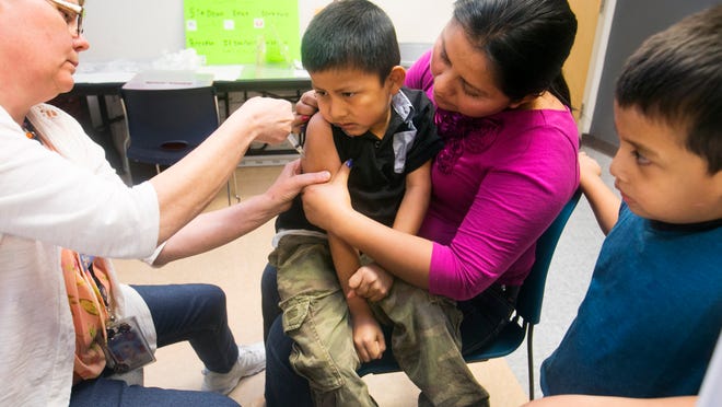Maricopa County nurse Diane Dickinson administers a measles vaccine to Jose Nix, 6, of Phoenix as mom Rosaura and brother Ada, 4, watch.